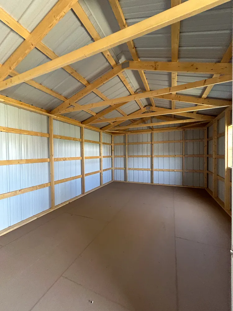 Inside a portable garage with white walls, wood framing and a plywood floor