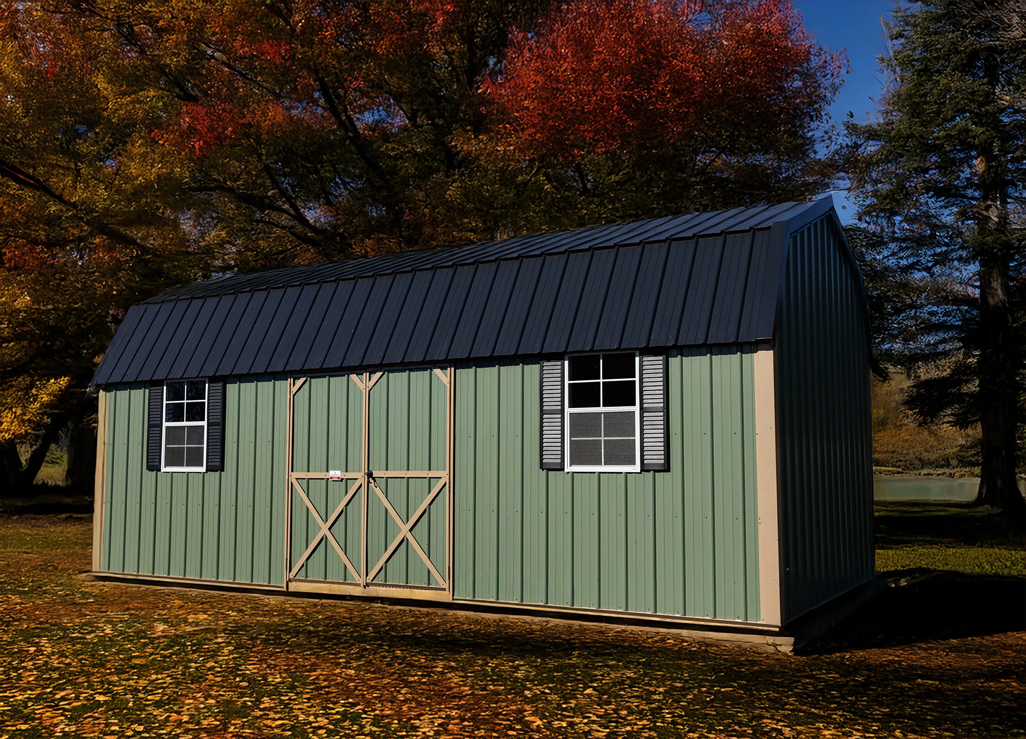 Long sage-green lofted metal shed with a dark roof among fallen leaves