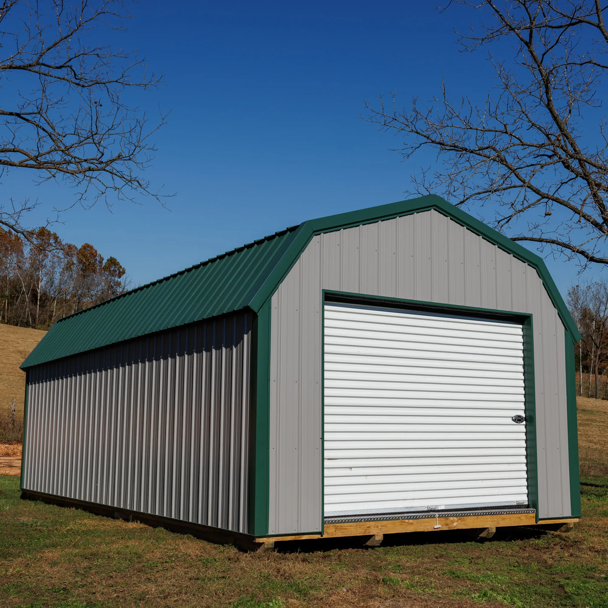Lofted metal garage with green trim, gray siding and a white roll-up door
