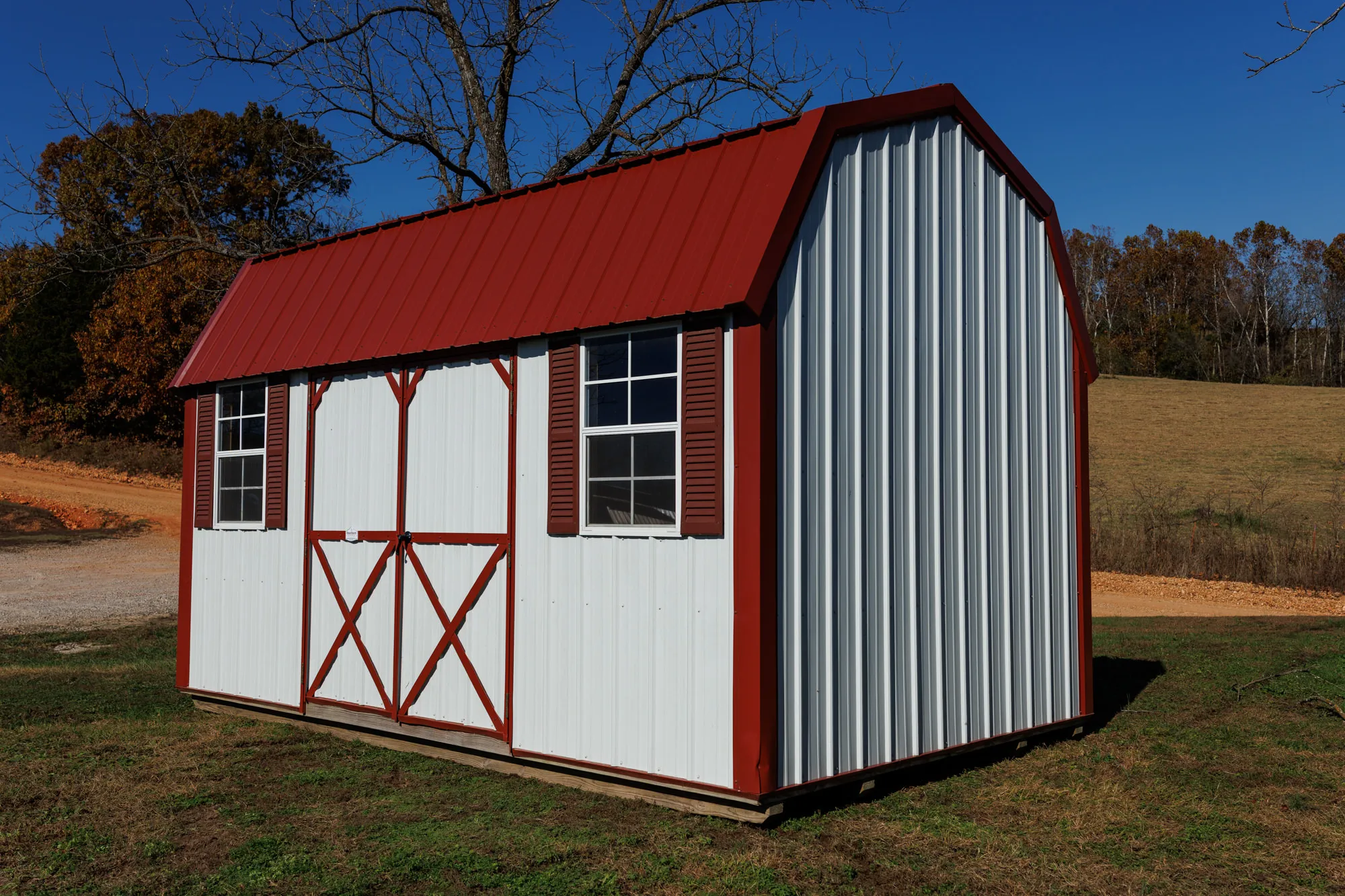 White lofted barn with a red metal roof, red X-braced doors and shuttered windows