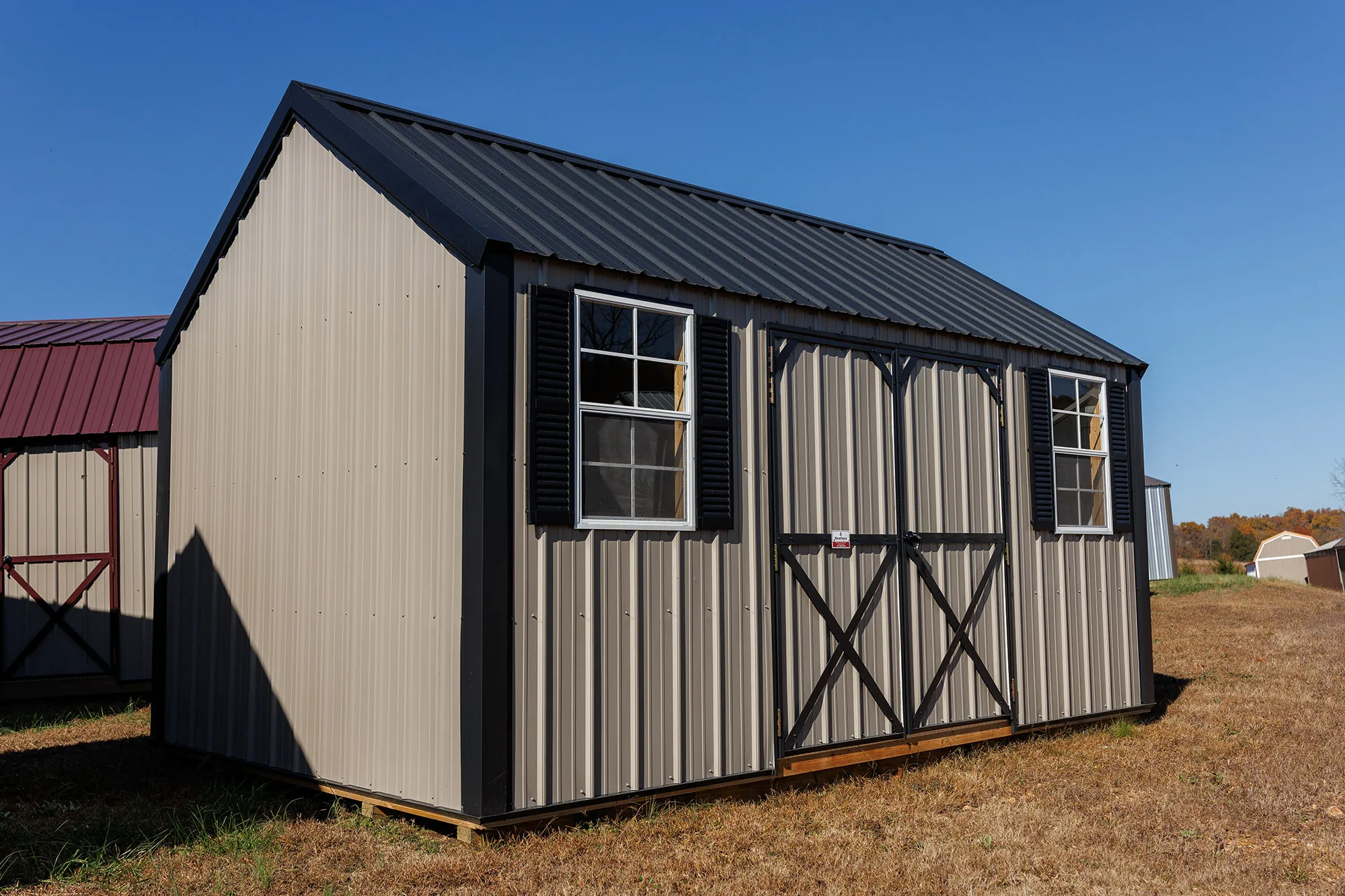 Gray metal-sided shed with black X-braced doors and shuttered windows