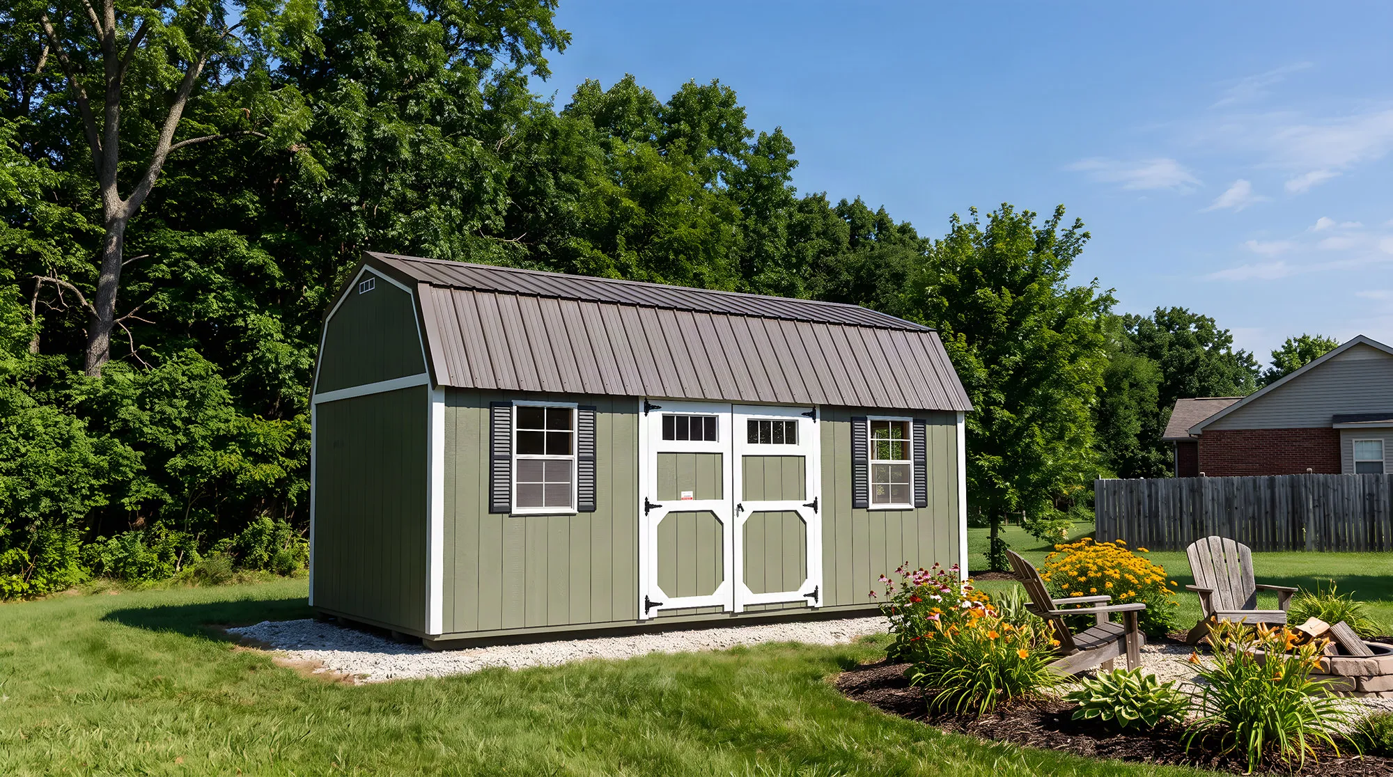 Sage-green lofted garden shed with white doors and a gray roof in a landscaped yard